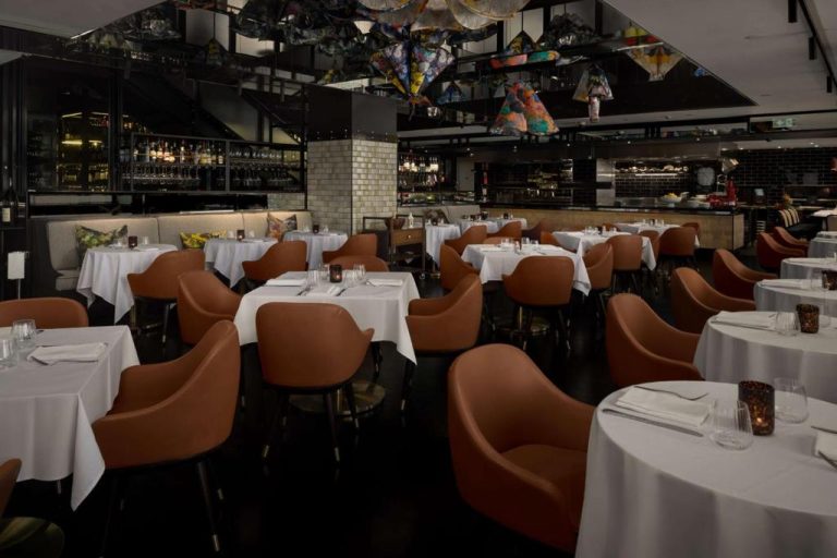 Elegante restaurante del QT Sydney con sillas de cuero marrón, mesas con manteles blancos y decoración artística en el techo