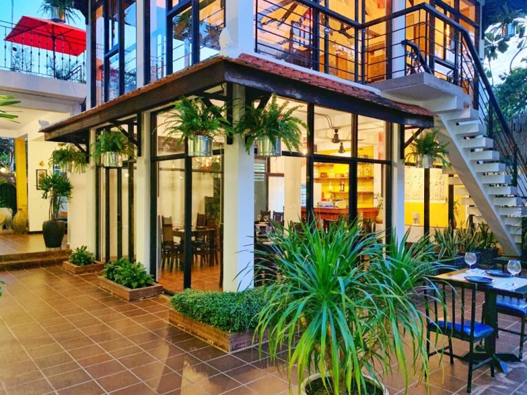 Terraza exterior con jardín tropical y restaurante acristalado del hotel The Bliss Angkor en Siem Reap