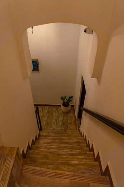 Escaleras interiores de madera con arco decorativo y planta tropical en el Hotel Aurelia Zanzibar