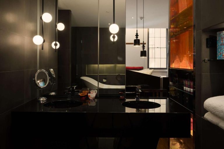 Baño de lujo con encimera negra y espejos iluminados en el QT Sydney Hotel