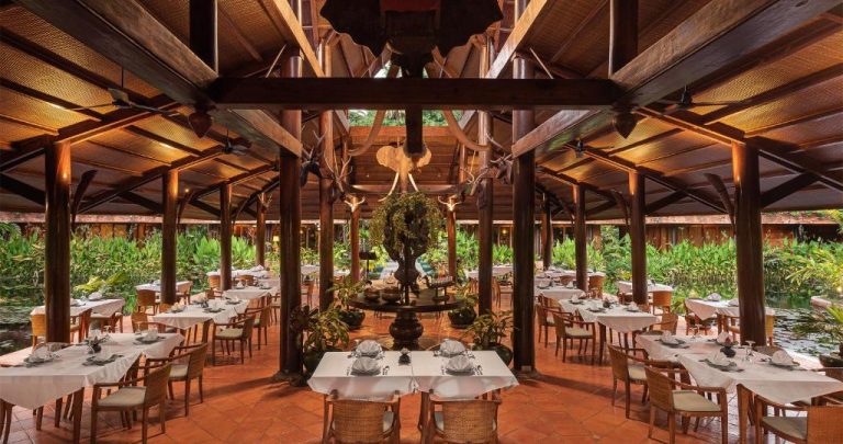 Restaurante abierto con mesas blancas y jardín tropical en Angkor Village Hotel, Small Luxury Hotels