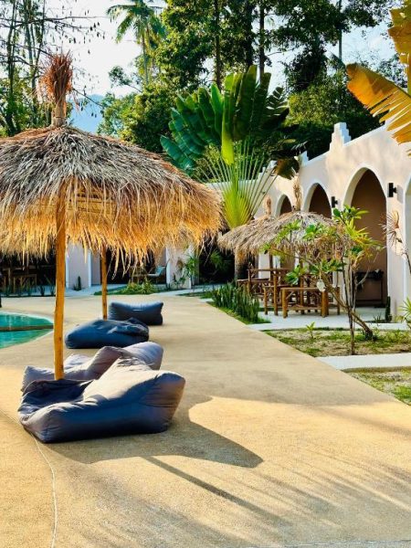 Zona de relax con tumbonas y sombrillas de palma junto a la piscina del Zibá Home Suites rodeada de vegetación tropical