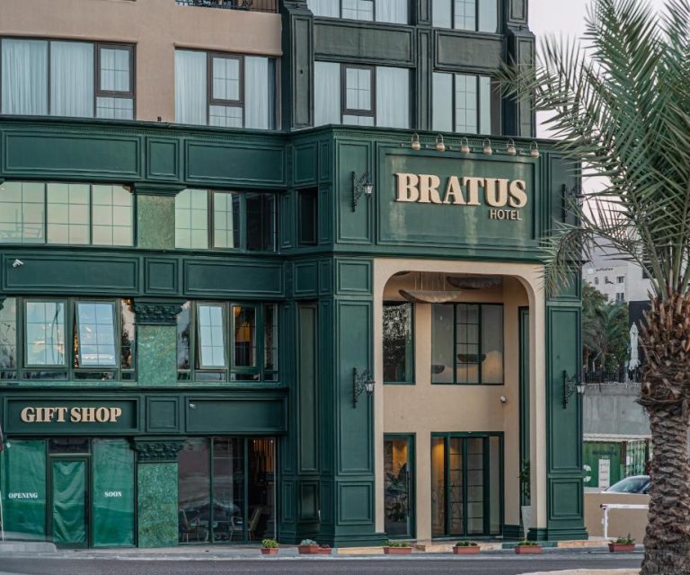 Fachada exterior del Bratus Hotel con entrada principal, acabados en verde oscuro y tienda de regalos