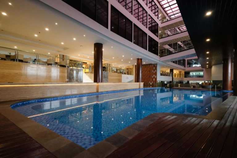 Piscina interior iluminada del Dream of Aventus Hotel Kuta con vistas al atrio y múltiples plantas