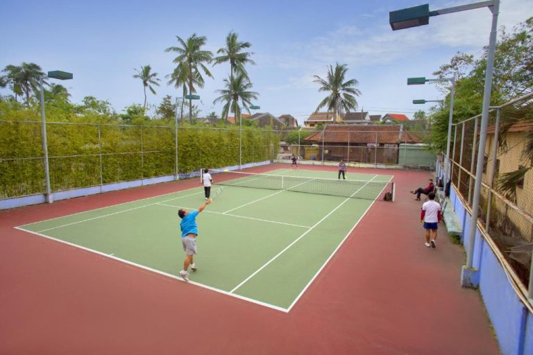 Pista de tenis exterior con jugadores en el Hoi An Historic Hotel rodeada de palmeras tropicales