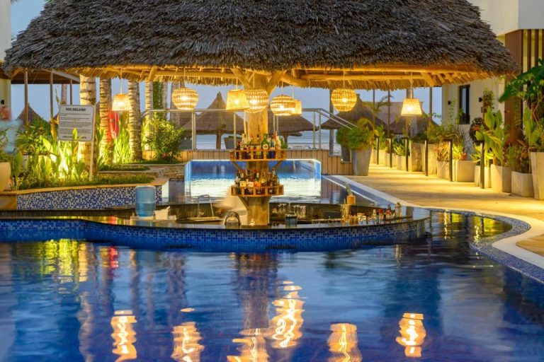 Bar en la piscina con techo de paja y luces cálidas del TOA Hotel & Spa Zanzibar al atardecer