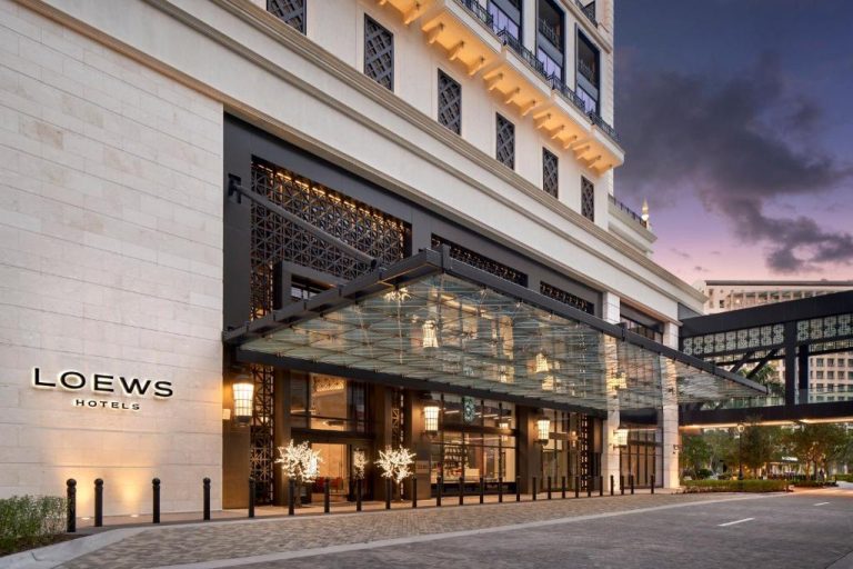 Entrada principal del Loews Coral Gables Hotel con marquesina de cristal y fachada iluminada al atardecer
