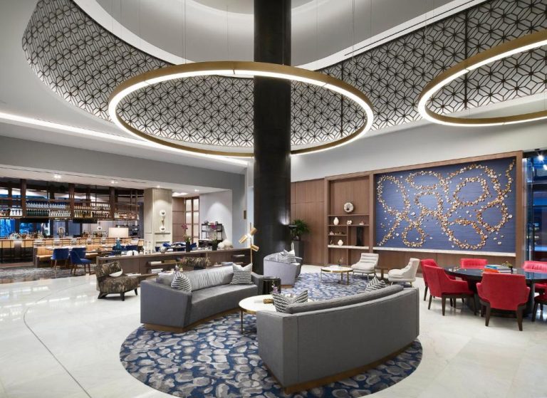 Elegante lobby lounge del Loews Coral Gables Hotel con sofás grises, techo decorativo y bar