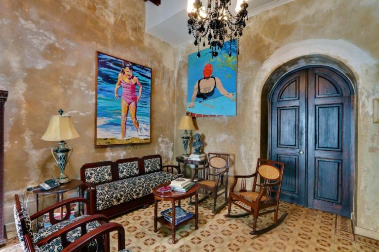 Salón colonial del Villa Herencia Hotel con arte local, muebles de época y puerta arqueada de madera oscura