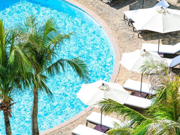 Piscina exterior circular con tumbonas y sombrillas blancas rodeada de palmeras en Hotel Nikko Alivila