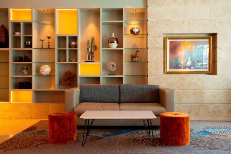 Zona lounge del Sheraton Athlone Hotel con sofá, pufs naranja y estantería decorativa iluminada