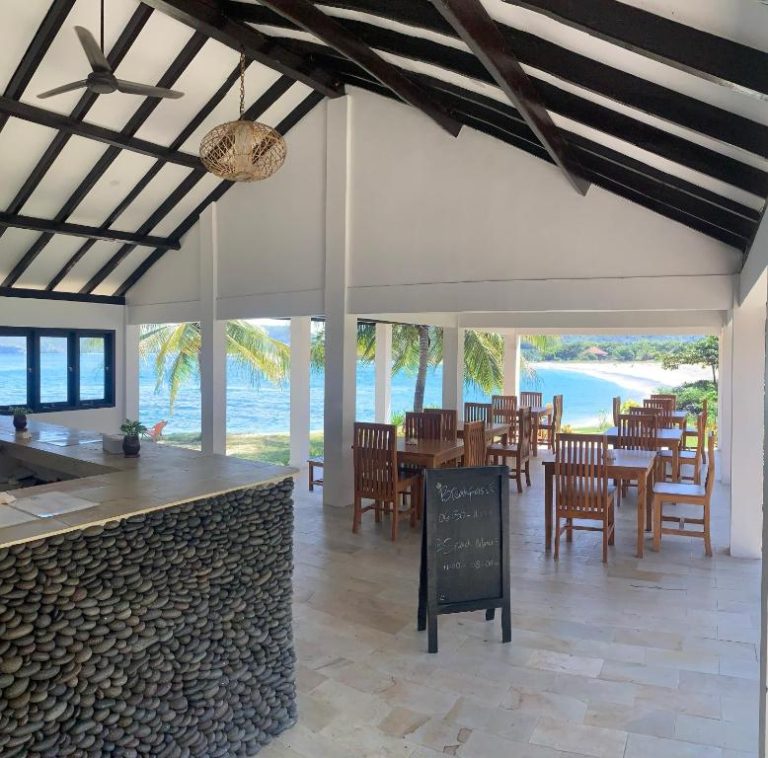 Restaurante frente al mar con mesas de madera y vistas a la playa en Balong Balong Surf Bungalows