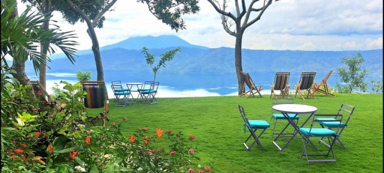 Jardín con mesas y sillas frente al lago y montañas en Hotel El Guayacán
