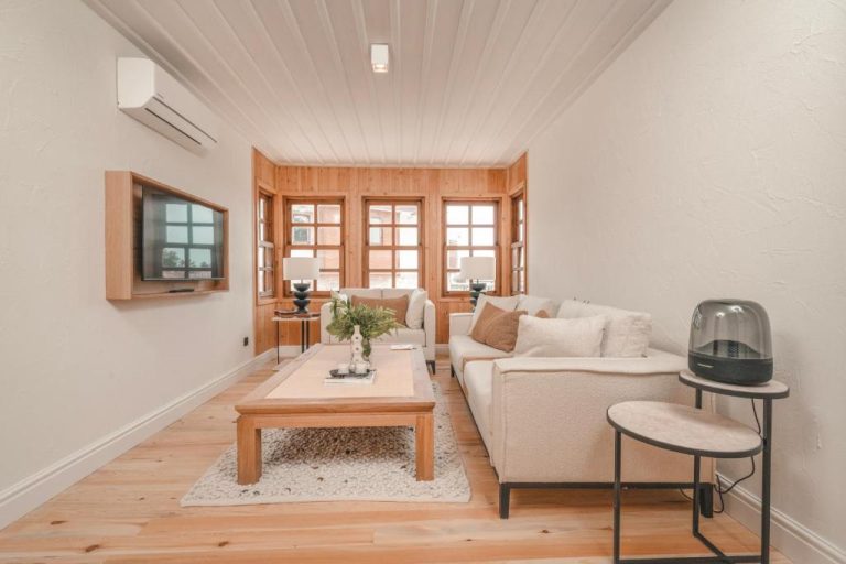 Salón luminoso con sofá blanco, suelo de madera y ventanas de pino en 6 Rooms by Zula