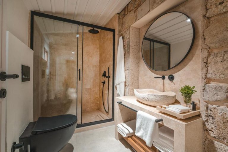 Baño de piedra natural con ducha de lluvia y lavabo de travertino en 6 Rooms by Zula