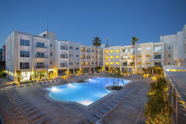 Piscina exterior iluminada del Mayfair Hotel rodeada de tumbonas y edificios blancos al atardecer