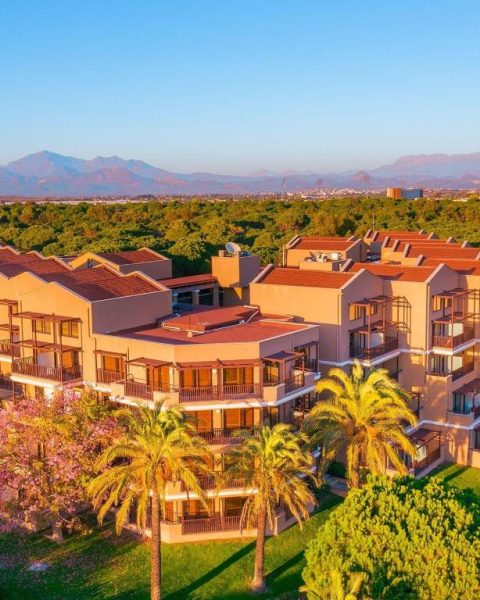 Vista aérea del Asteria Family Resort Belek con jardines, palmeras y montañas al fondo