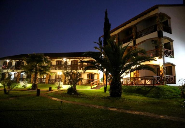 Fachada exterior iluminada de noche del hotel Termas Posada del Siglo XIX con jardines y palmeras