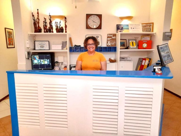 Recepcionista sonriente en el mostrador de recepción del Hotel MiraBela con decoración tropical