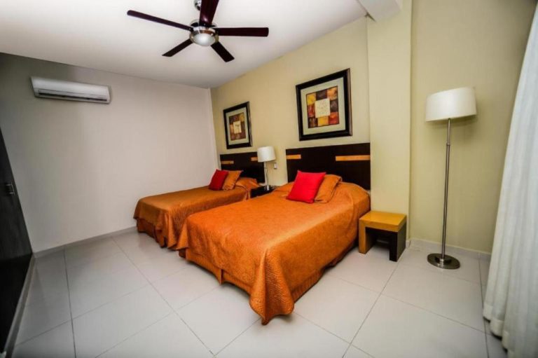 Habitación doble con camas naranjas y cojines rojos en Hotel Encanto Riviera, con ventilador de techo y aire acondicionado
