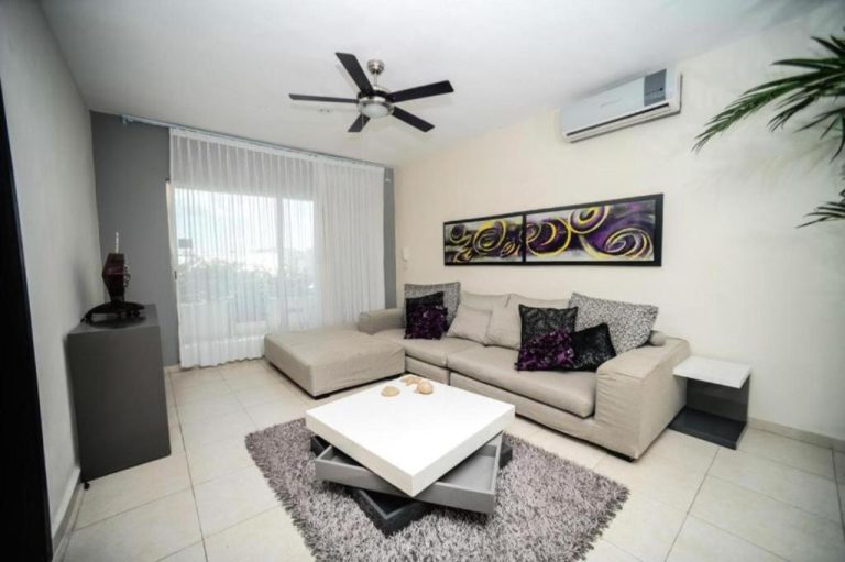Sala de estar moderna con sofá gris, mesa de centro blanca y aire acondicionado en Encanto Riviera