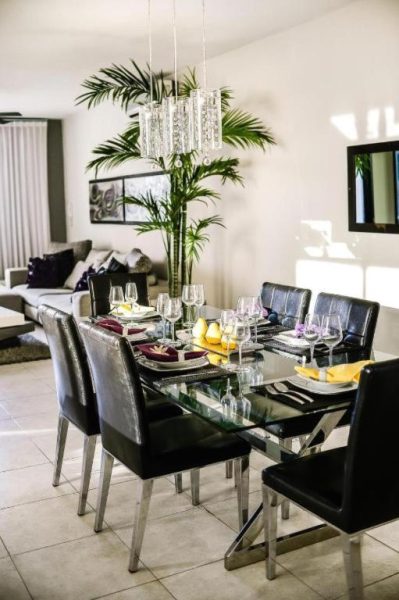 Comedor elegante con mesa de cristal y sillas negras en Encanto Riviera, decorado con lámpara de araña