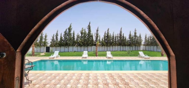 Piscina exterior con tumbonas y jardín arbolado en Auberge Dar Laazouzi vista desde arco de entrada
