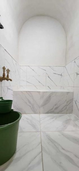 Baño tradicional con azulejos de mármol blanco y grifo dorado en Auberge Dar Laazouzi