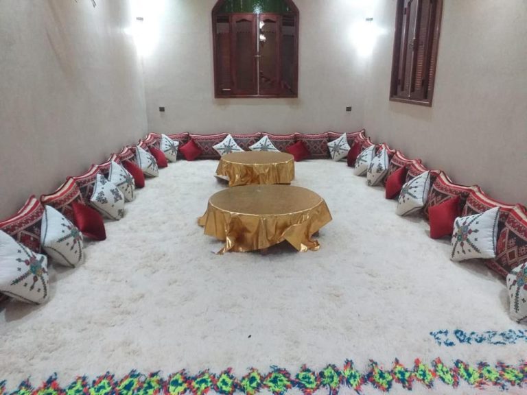 Salón árabe tradicional con cojines decorativos y mesas doradas en Auberge Dar Laazouzi