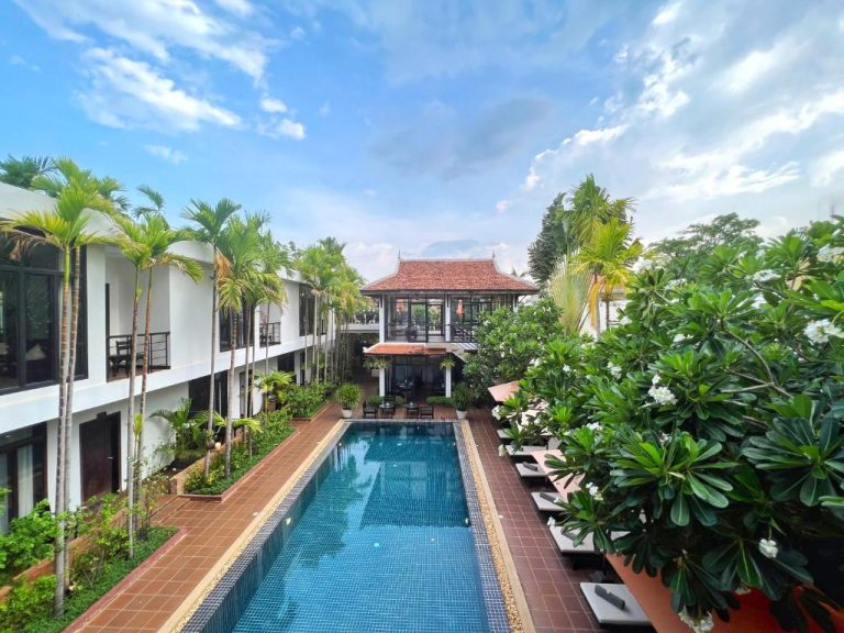 Piscina exterior rodeada de palmeras y jardines tropicales en The Bliss Angkor Hotel