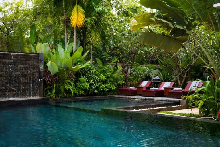 Piscina exterior con cascada y tumbonas rojas rodeada de jardín tropical en Sokkhak Boutique Resort & Spa