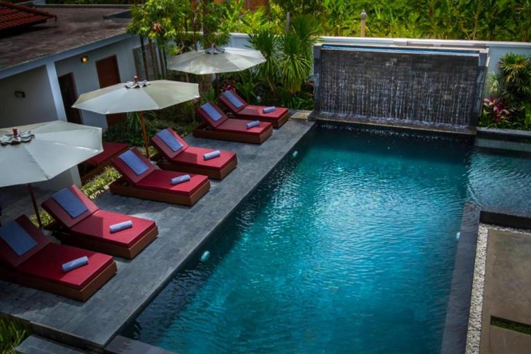 Piscina exterior con cascada y tumbonas rojas del Sokkhak Boutique Resort & Spa rodeada de jardín tropical