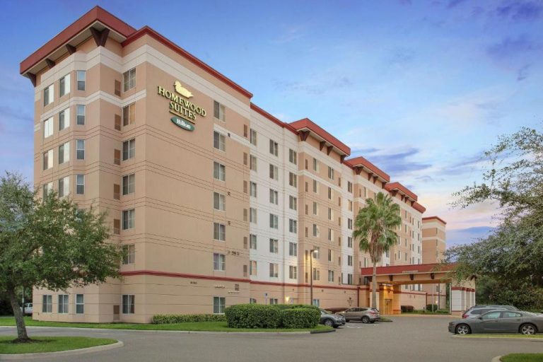 Fachada exterior del Homewood Suites by Hilton Tampa-Brandon con aparcamiento y palmeras al atardecer