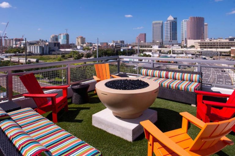 Terraza con fogón central y sillas coloridas en Home2 Suites by Hilton Tampa Downtown con vistas al skyline