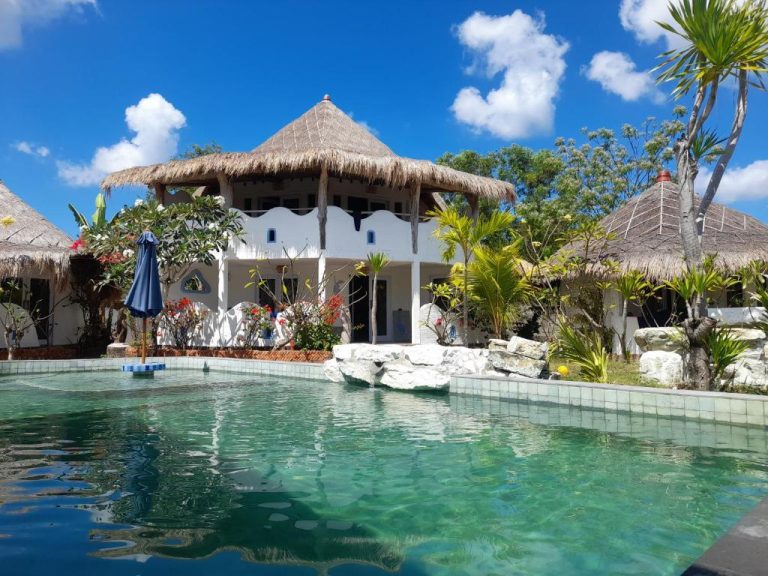 Piscina exterior con aguas cristalinas frente a los bungalows con techo de paja del SHAYA Cottage