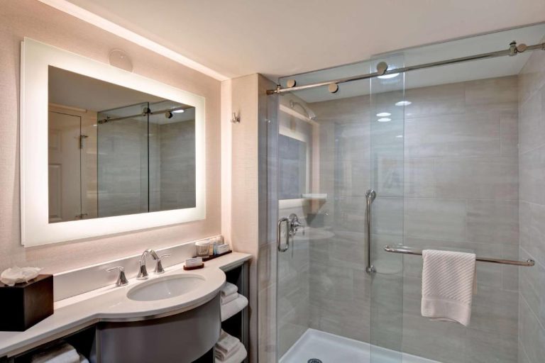 Baño moderno con ducha de cristal y lavabo iluminado en Embassy Suites by Hilton Orlando Downtown