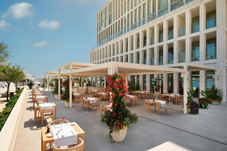 Terraza restaurante exterior con mesas y flores rojas del Hotel Ambasador frente al mar