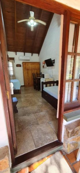 Interior de cabaña rústica con cama, techo de madera y ventilador en Termas Posada del Siglo XIX