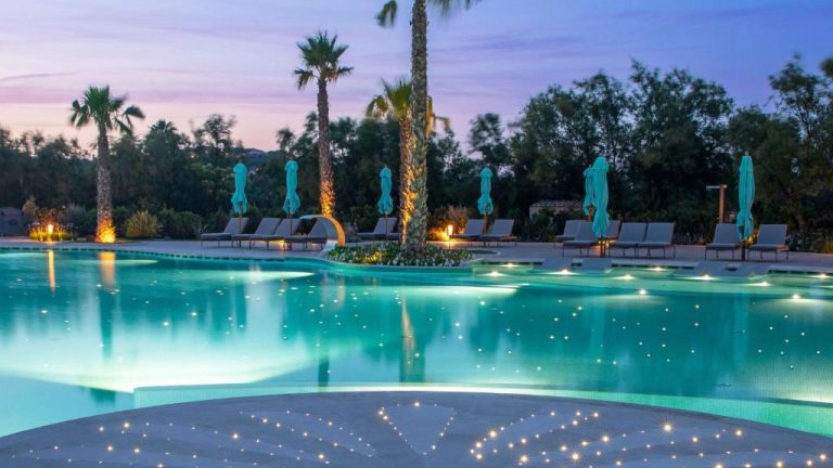 Piscina exterior iluminada al atardecer del Abi d'Oru Sardinian Beach Resort & Spa en Cerdeña