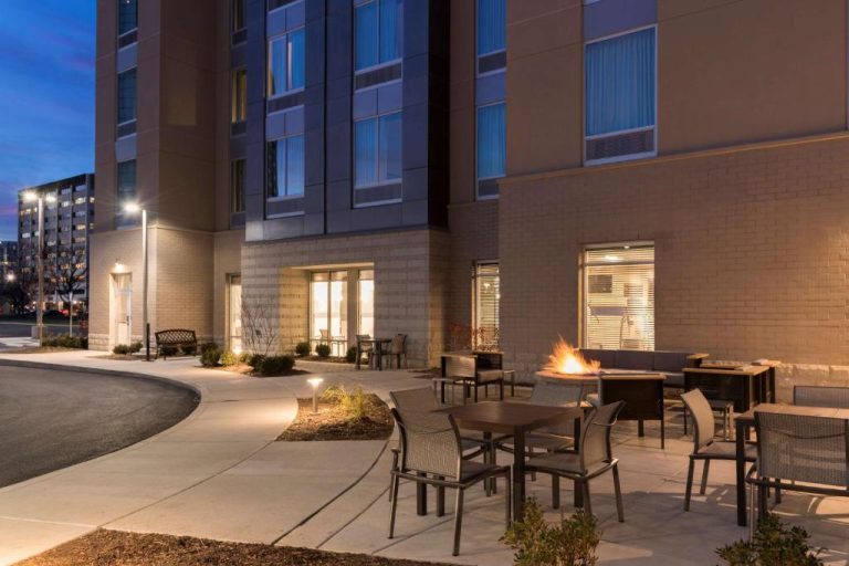 Terraza exterior con hoguera y mesas del Hampton Inn & Suites Indianapolis-Keystone al atardecer