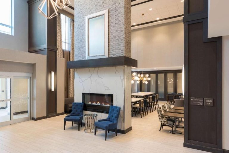 Lobby con chimenea y zona de desayuno del Hampton Inn & Suites Indianapolis-Keystone con sillones azules