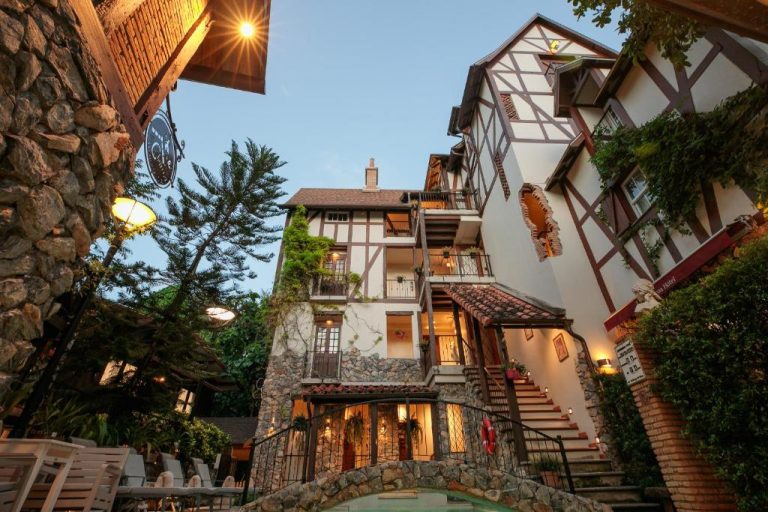 Fachada exterior de estilo Tudor del Le Charcoa Hotel con jardines, iluminación nocturna y terrazas