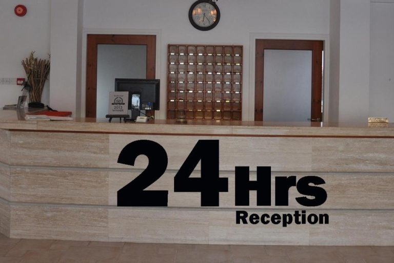 Recepción abierta 24 horas del Tasmaria Aparthotel con mostrador de mármol y reloj de pared
