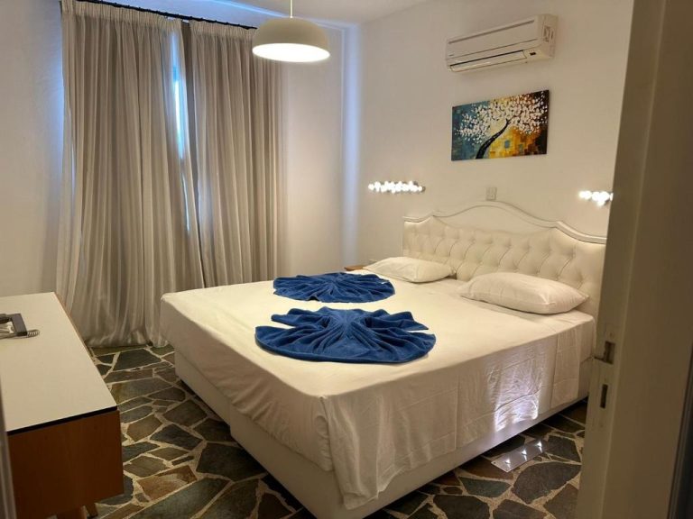 Habitación doble con cama matrimonial blanca y toallas decorativas azules en Tasmaria Aparthotel