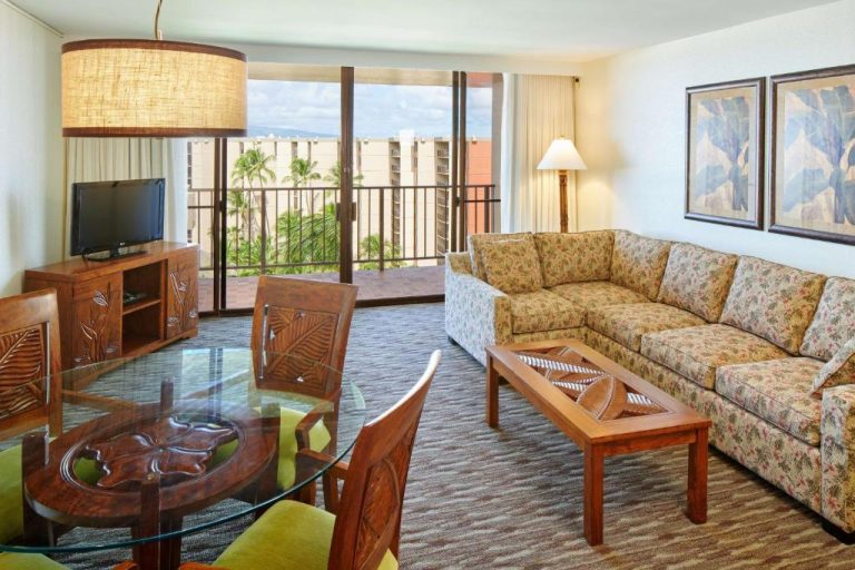 Sala de estar con sofá floral, mesa de cristal y balcón con vistas a palmeras en Aston Kaanapali Shores