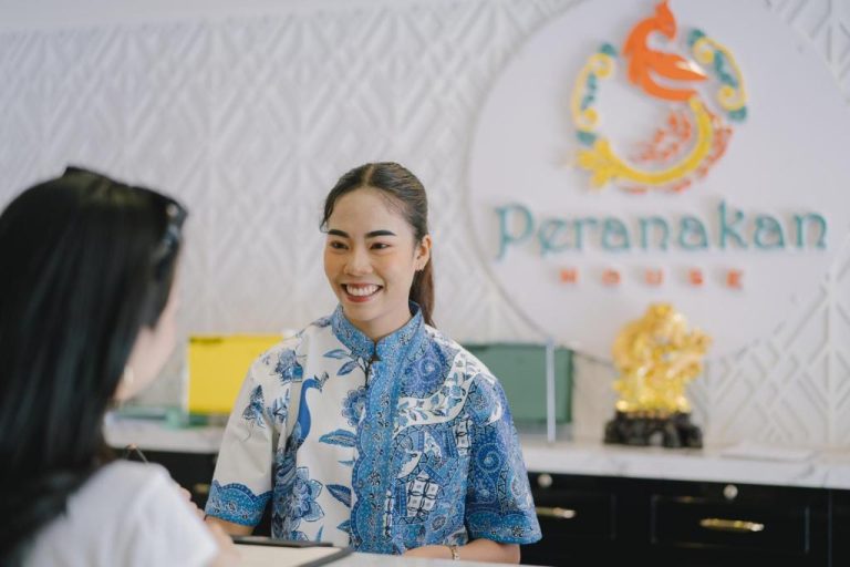 Recepcionista sonriente atendiendo a huésped en el mostrador de recepción del Peranakan House
