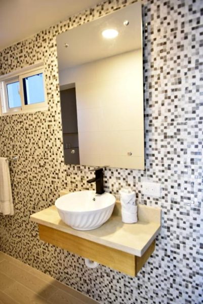 Baño moderno con lavabo sobre encimera de madera y pared de mosaico en Halibut Hotel