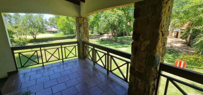Terraza cubierta con columnas de piedra y vistas al jardín verde en Termas Posada del Siglo XIX