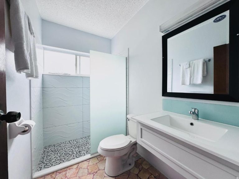 Baño privado con ducha, lavabo y espejo en Toby's Resort, decorado en tonos blancos y azules