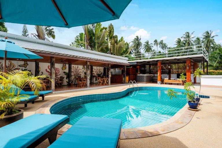 Piscina exterior con tumbonas azules y bar en Tropical Heavens Garden Samui rodeada de palmeras tropicales